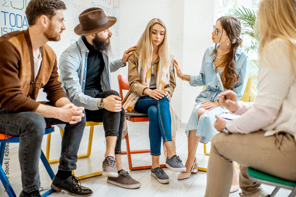 Young woman crying during the psychological therapy with group of people supporting her in the offic