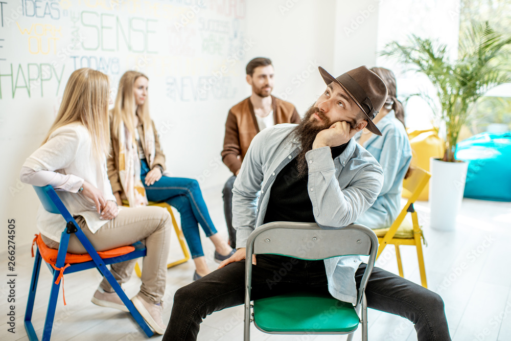 Portrait of a handsome man sitting in a circle with group of people during the psychological trainin