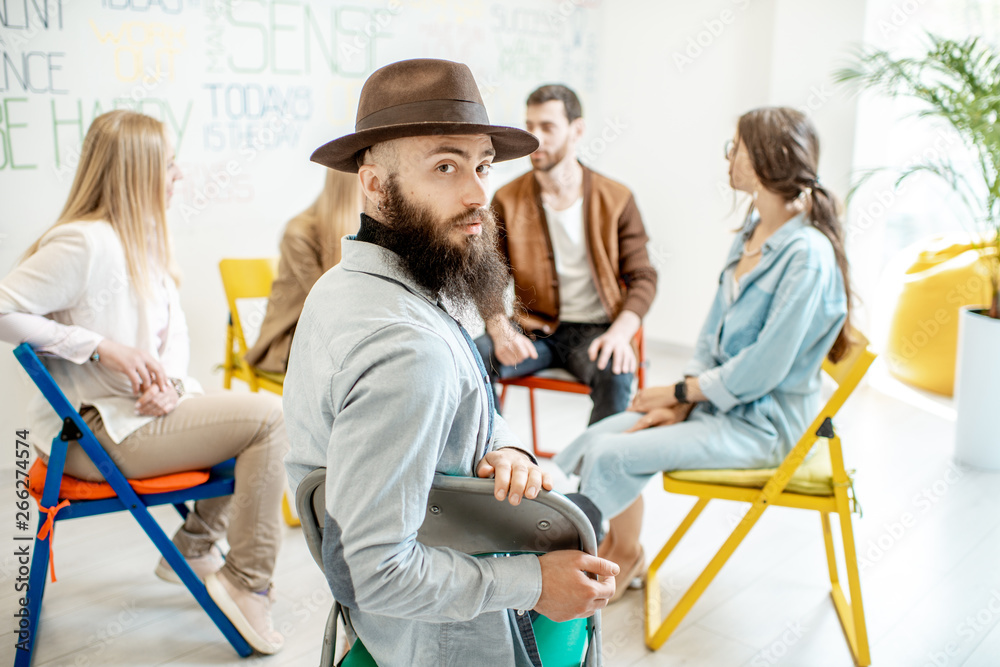 Portrait of a handsome man sitting in a circle with group of people during the psychological trainin