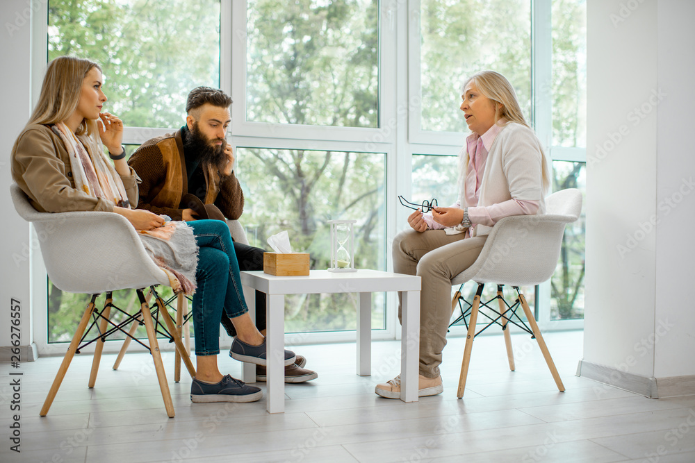 Young couple having misunderstandings during the psychological counseling with senior female psychol