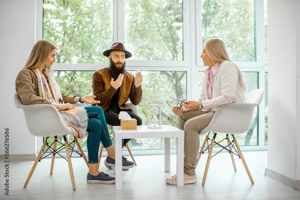 Young couple having misunderstandings during the psychological counseling with senior female psychol