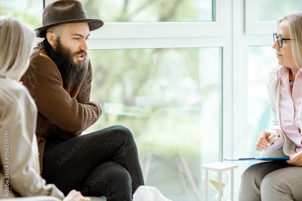 Young couple having misunderstandings during the psychological counseling with senior female psychol