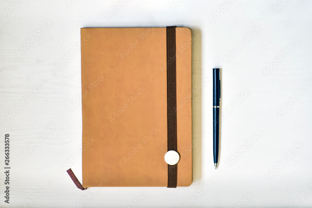 Notebook (beige, brown), lying on a white table, illuminated by natural muted daylight.