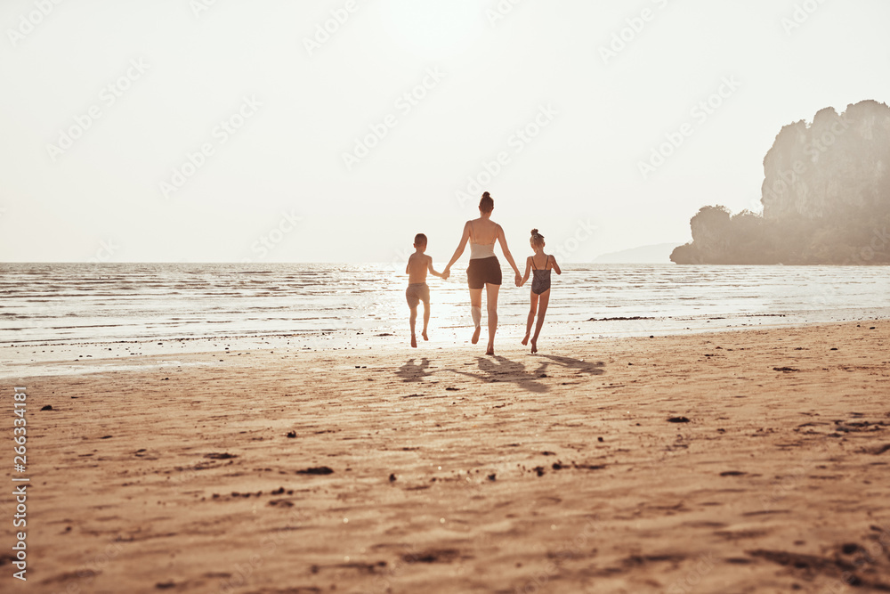 Mother and children holding hands and skipping along a beach