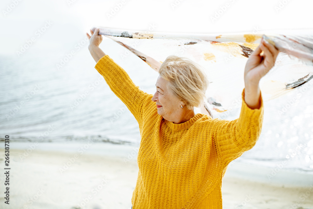 沙滩上，一位身穿鲜艳毛衣、头顶围巾享受海风的资深女士