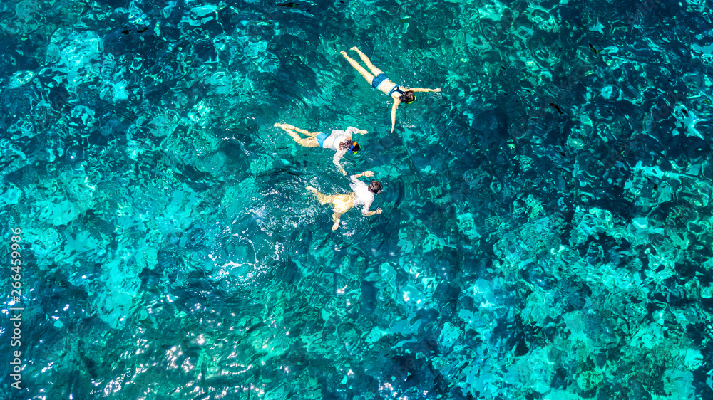 Aerial top view of family snorkeling from above, mother and kids snorkelers swimming in a clear trop