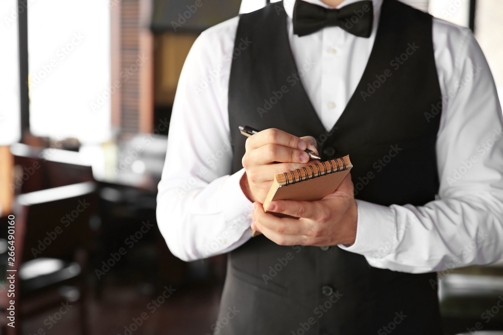 Young male waiter with notebook in restaurant, closeup