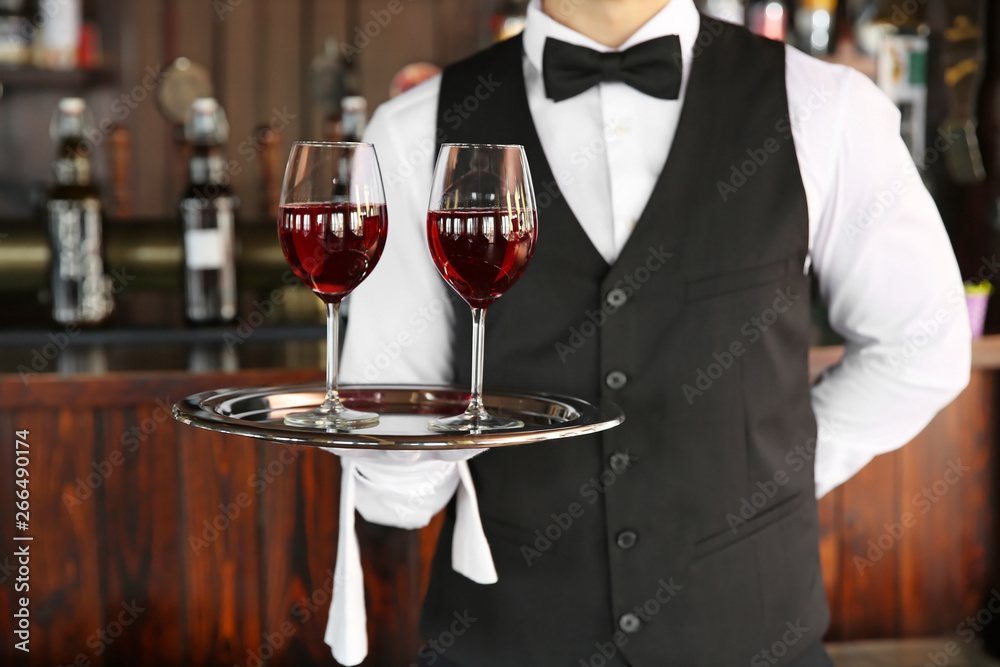 Young male waiter with glasses of wine in restaurant