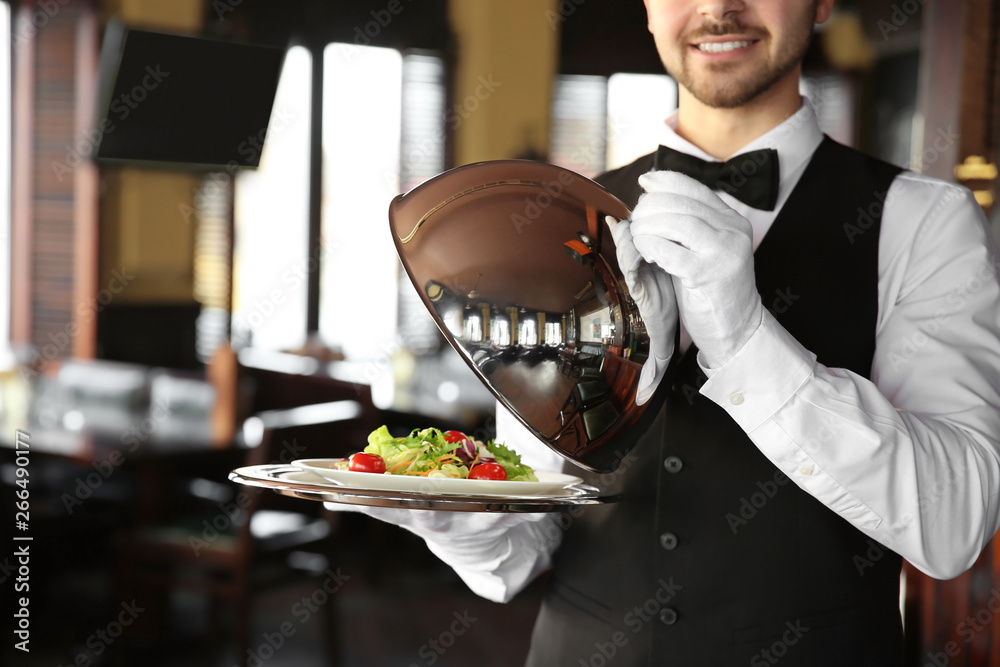 Young male waiter with salad in restaurant