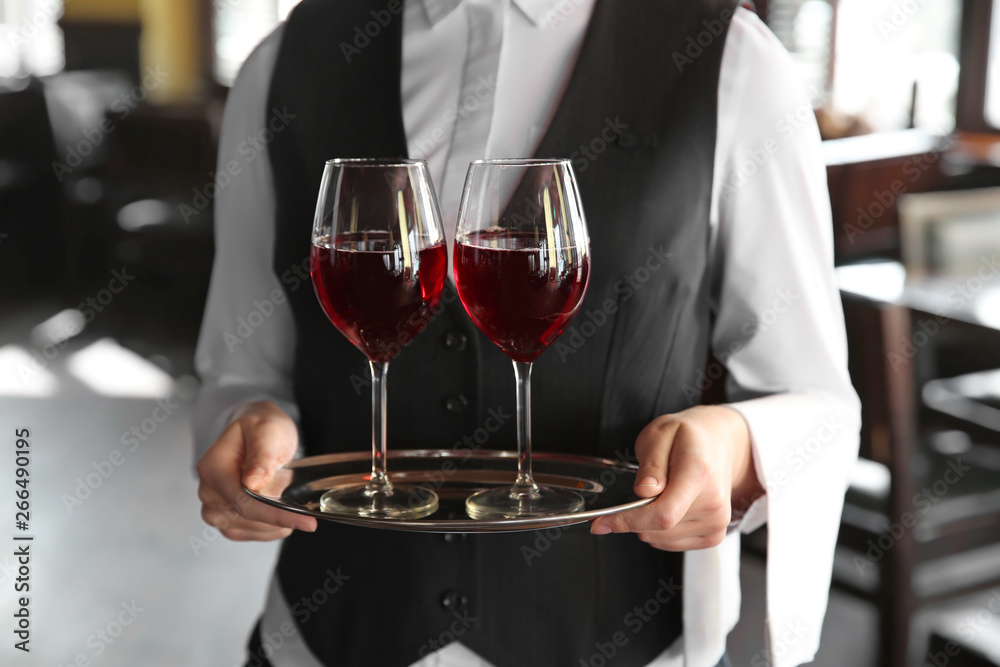 Young female waiter with glasses of wine in restaurant, closeup