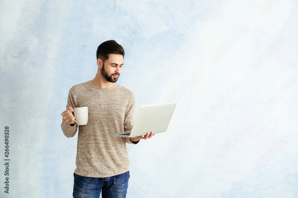 Male programmer with laptop and cup of coffee on color background