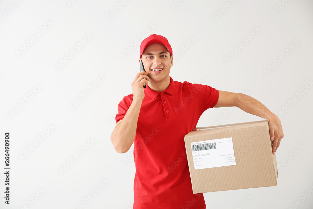 Delivery man with box talking by mobile phone on light background