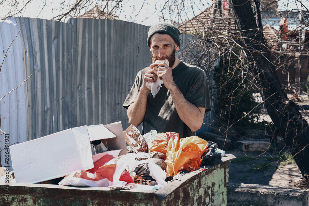 Poor homeless man near trash bin outdoors