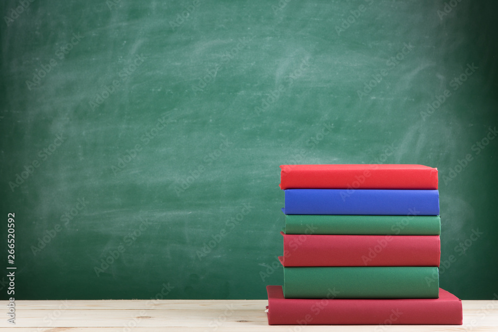 Education and reading concept - group of colorful books on the wooden table in the classroom, blackb