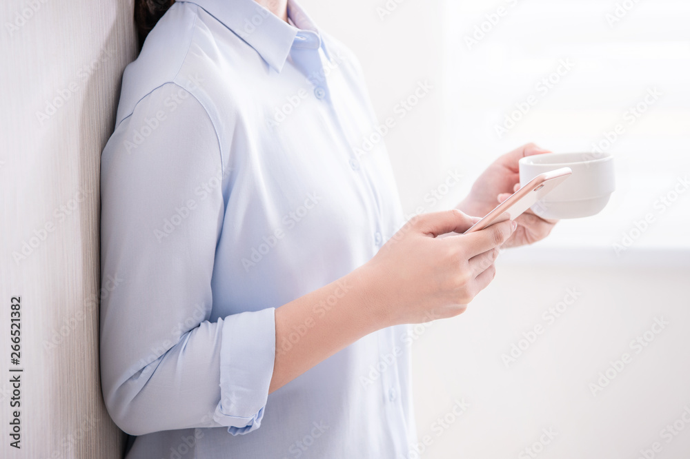 Side view of asia young business woman in blue shirt standing lying on the wall beside window drinki