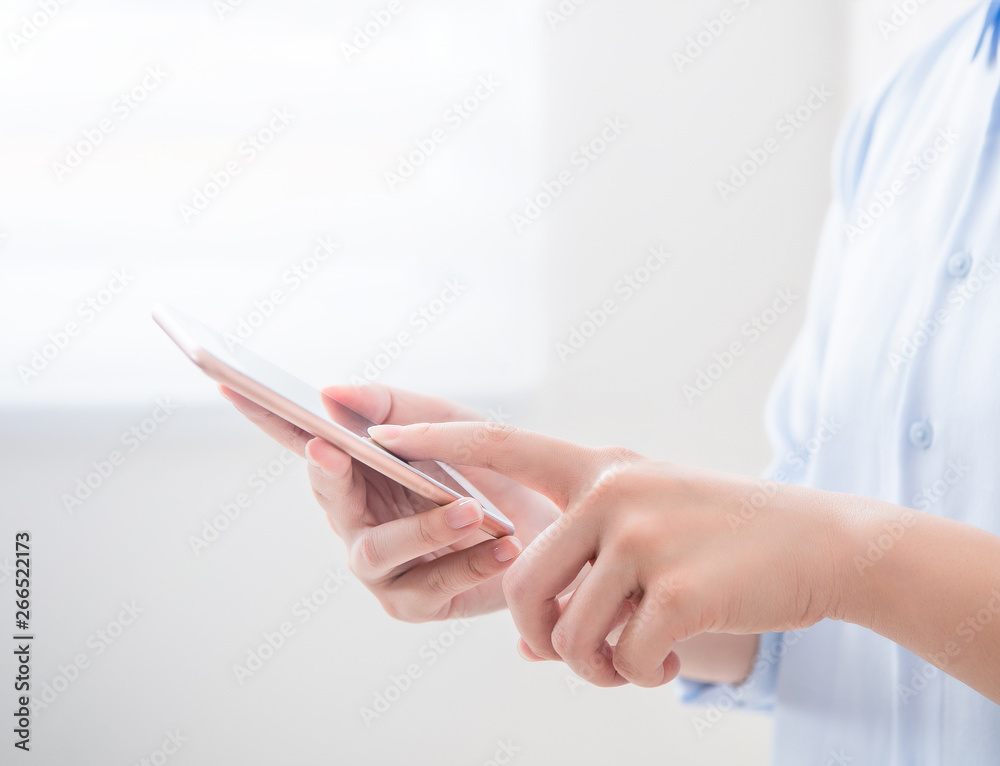 Side view of asia young business woman in blue shirt dress standing beside window and using smart ph