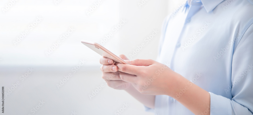 Side view of asia young business woman in blue shirt dress standing beside window and using smart ph