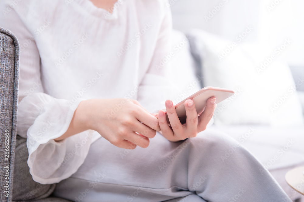 Side view of asia young woman in white sitting on sofa and using smart phone in bright living room, 