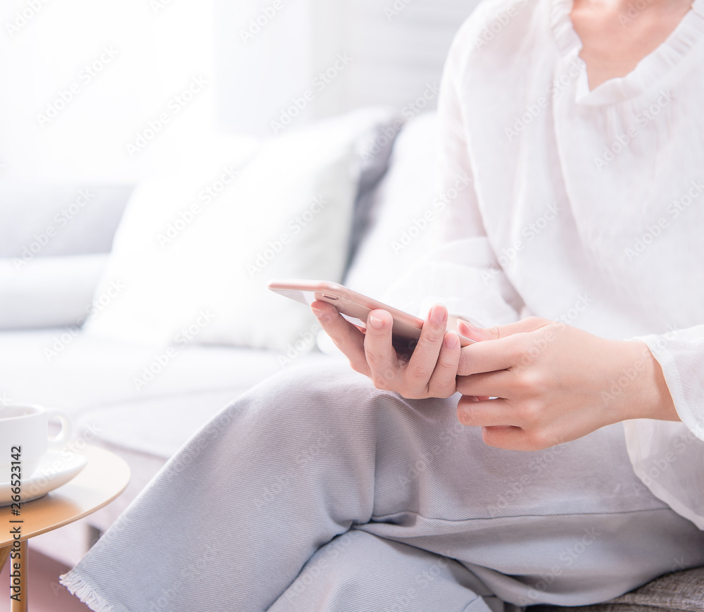 Side view of asia young woman in white sitting on sofa and using smart phone in bright living room, 