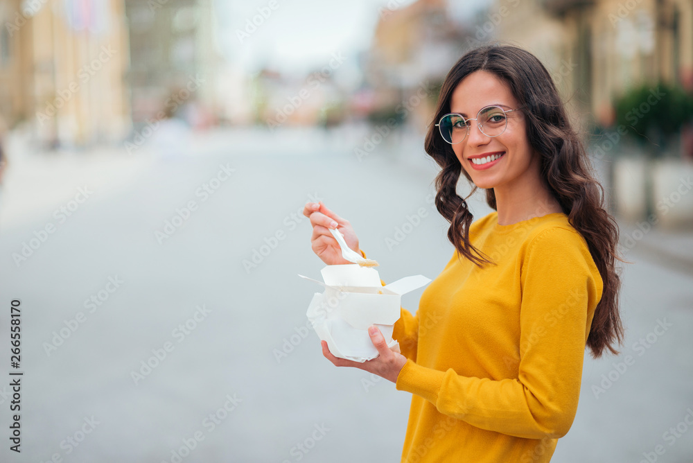 Smiling young woman eating takeout lunch in the city street, copy space.