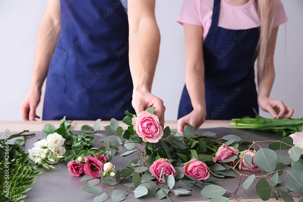 花艺师在灯光背景下在餐桌上制作花束