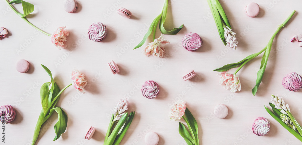 Flat-lay of sweet pink macaron cookies, lilac marshmallows and fresh spring flowers over pastel pink