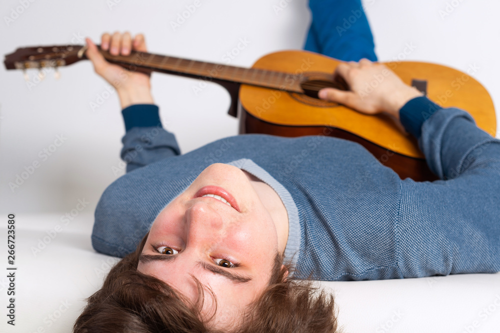 Happy young man lying back on sofa with guitar