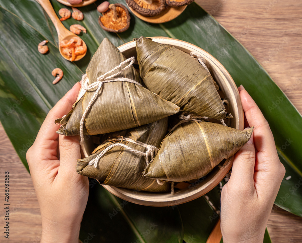 Zongzi, woman eating steamed rice dumplings on wooden table, food in dragon boat festival duanwu con