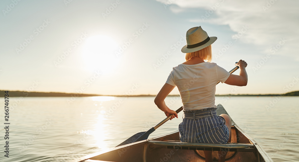 Young woman canoeing on a still lake in the summer