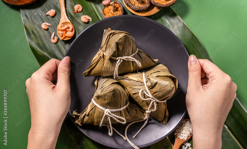 Zongzi, woman eating steamed rice dumplings on green table background, food in dragon boat festival 