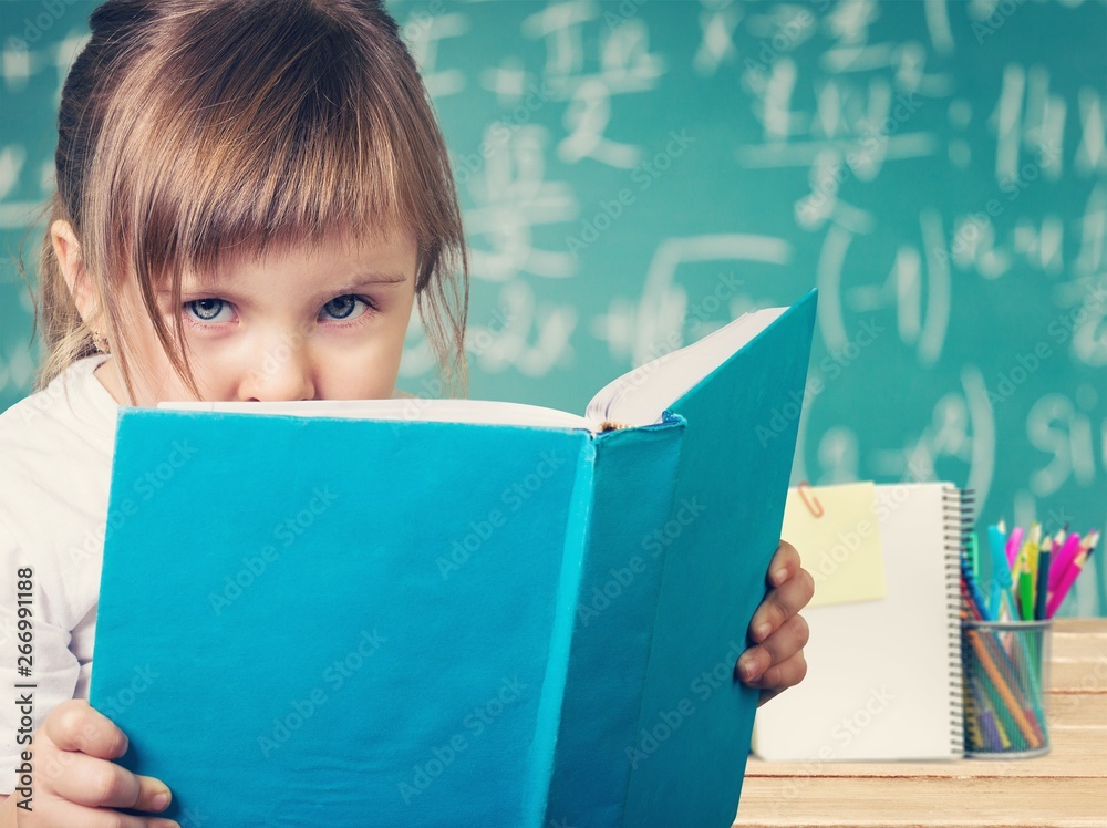 Little cute girl with books near green blackboard