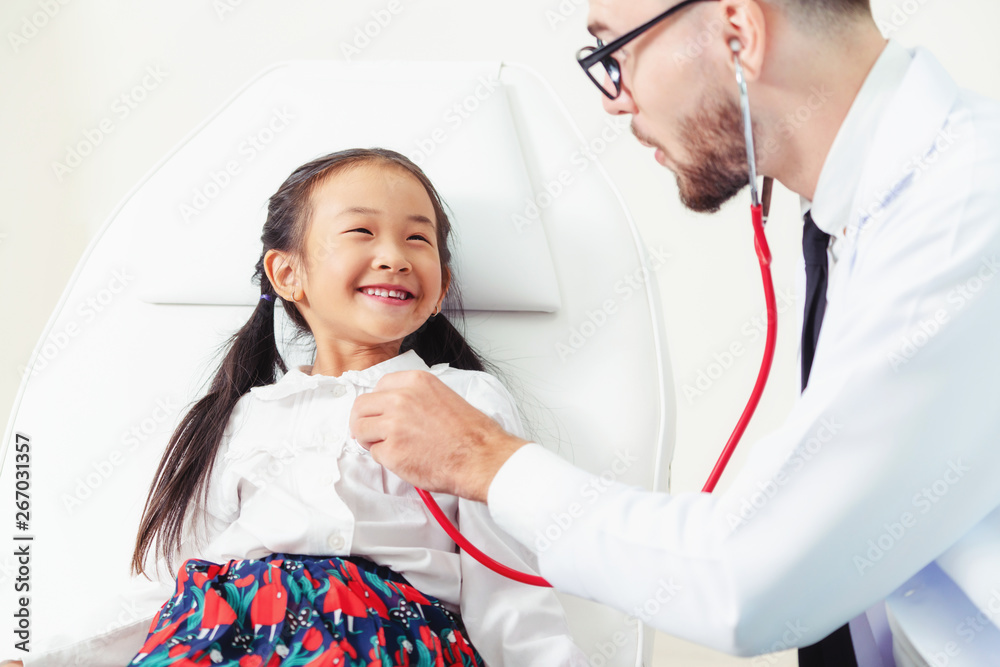 Young male doctor examining little kid in hospital office. The kid is happy and not afraid of the do