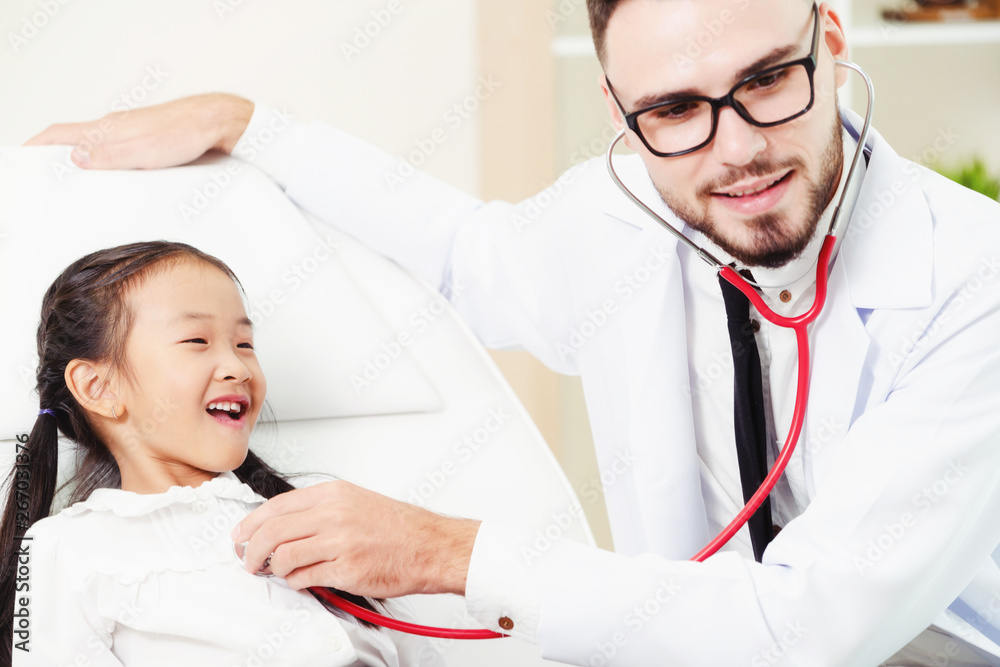 Young male doctor examining little kid in hospital office. The kid is happy and not afraid of the do