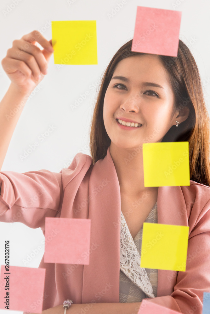 Happy businesswoman thinking creative ideas with sticky notes on glass wall at the office. Work plan