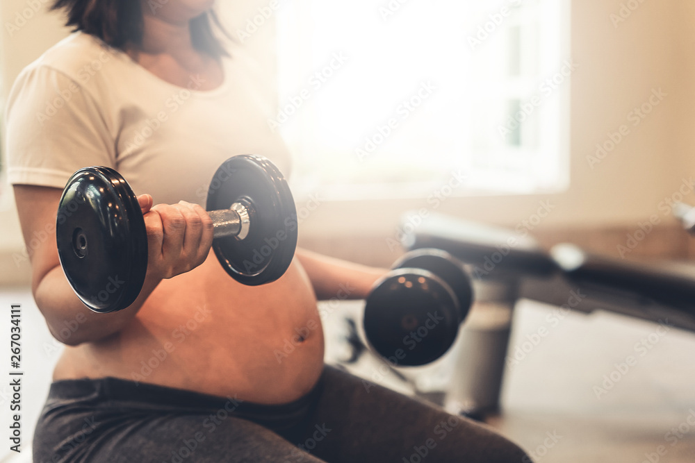 Active pregnant woman exercise in fitness center at yoga room. The young expecting mother holding ba