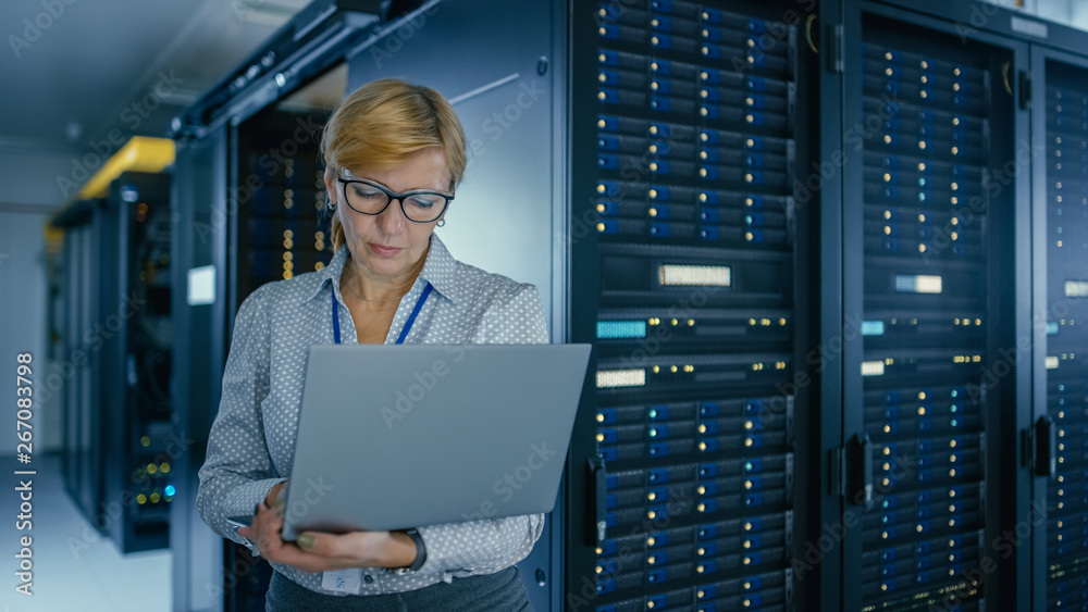 Portrait Shot In Data Center: Female IT Technician Running Maintenance Programme on a Laptop, Contro