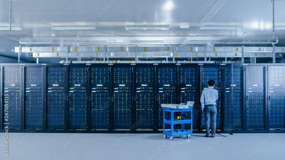 In the Data Center: IT Engineer Working with Server Racks Works with Opened Cabinet to Installs New 