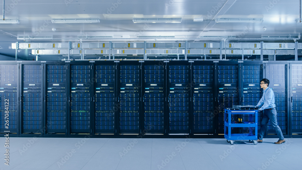 In the Modern Data Center: IT Technician Working with Server Racks, Pushes Cart Between Rows of Serv