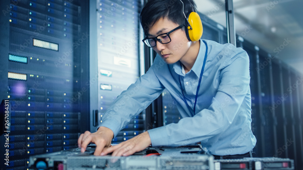 In the Modern Data Center: IT Engineer Wearing Protective Headphones Installs New Hardware for Serve