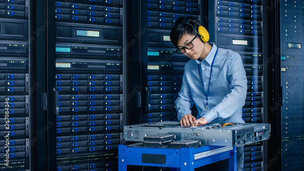 In Data Center: IT Engineer Wearing Protective Muffs Installs New Hardware for Server Rack. Speciali