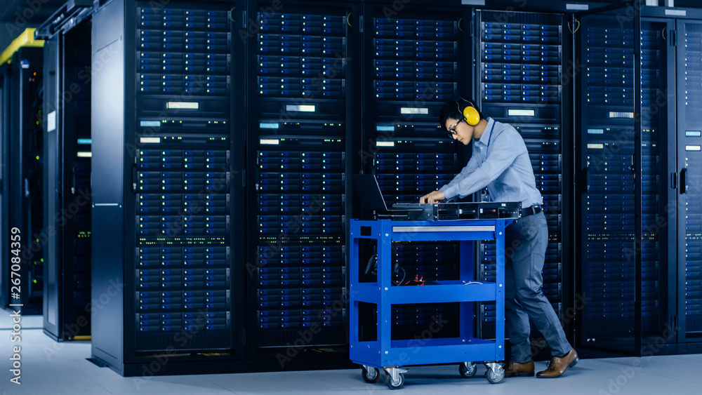 In Data Center: IT Engineer Wearing Protective Muffs Installs New Hardware for Server Rack. Speciali