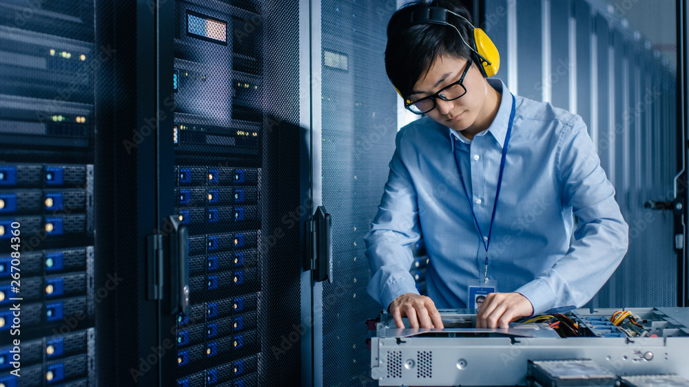 In Data Center: IT Engineer Wearing Protective Muffs Installs New Hardware for Server Rack. Speciali