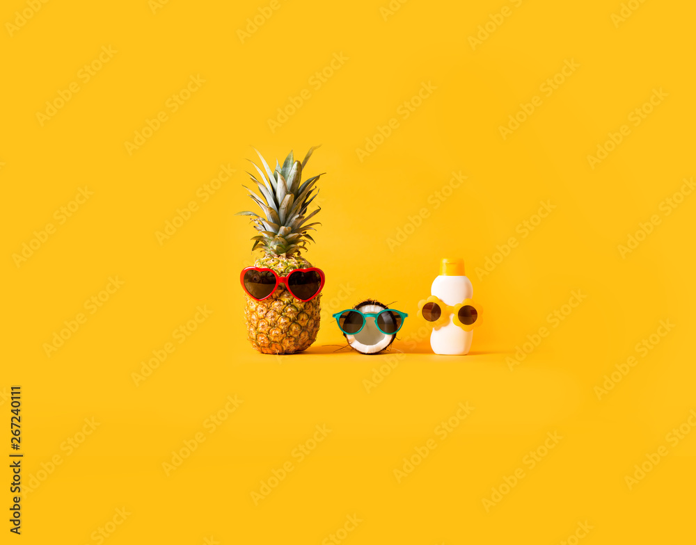 Pineapple and coconut wearing sunglasses with sunblock on a solid background