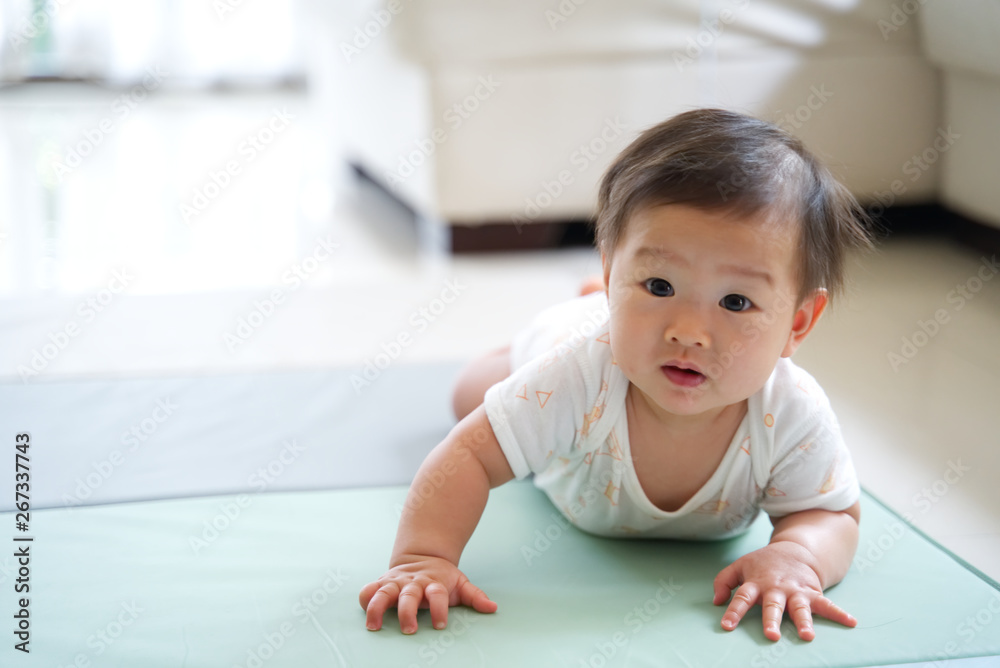 亚洲可爱的婴儿在家里柔软的地毯或垫子上爬行。孩子期待着她的妈妈留下来