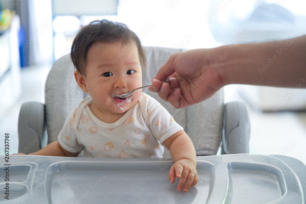 父亲在婴儿喂养座上给孩子喂粥。孩子喜欢吃这顿饭，面带微笑