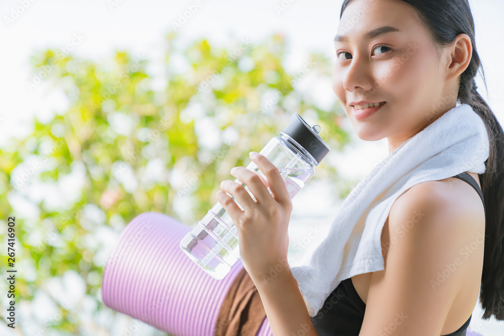 美丽的运动亚洲女性手持瑜伽垫和水瓶进行健康健身瑜伽锻炼