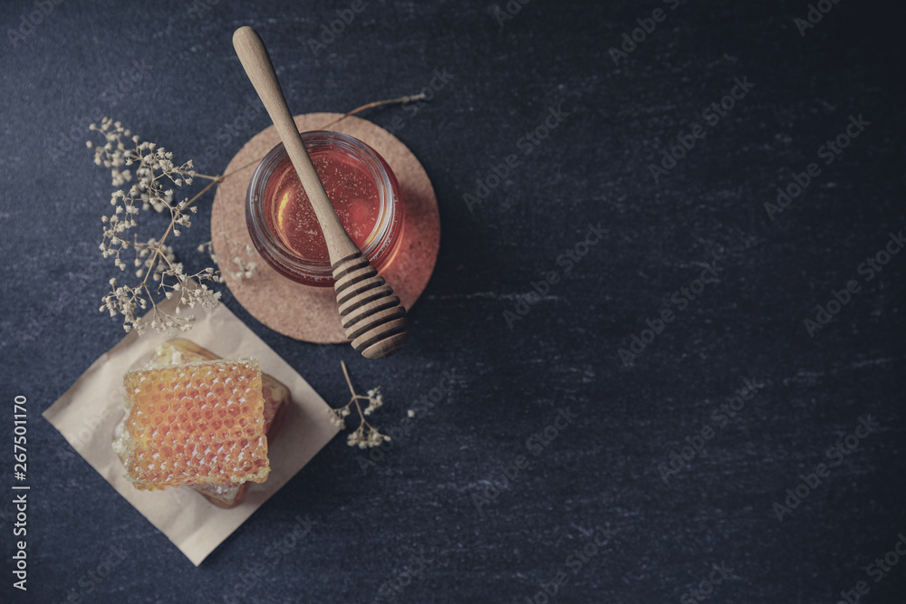 Honeycomb with honey dipper and dry flower on black background, bee products by organic natural ingr