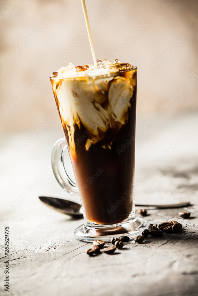 Ice coffee in a tall glass with cream poured over and coffee beans