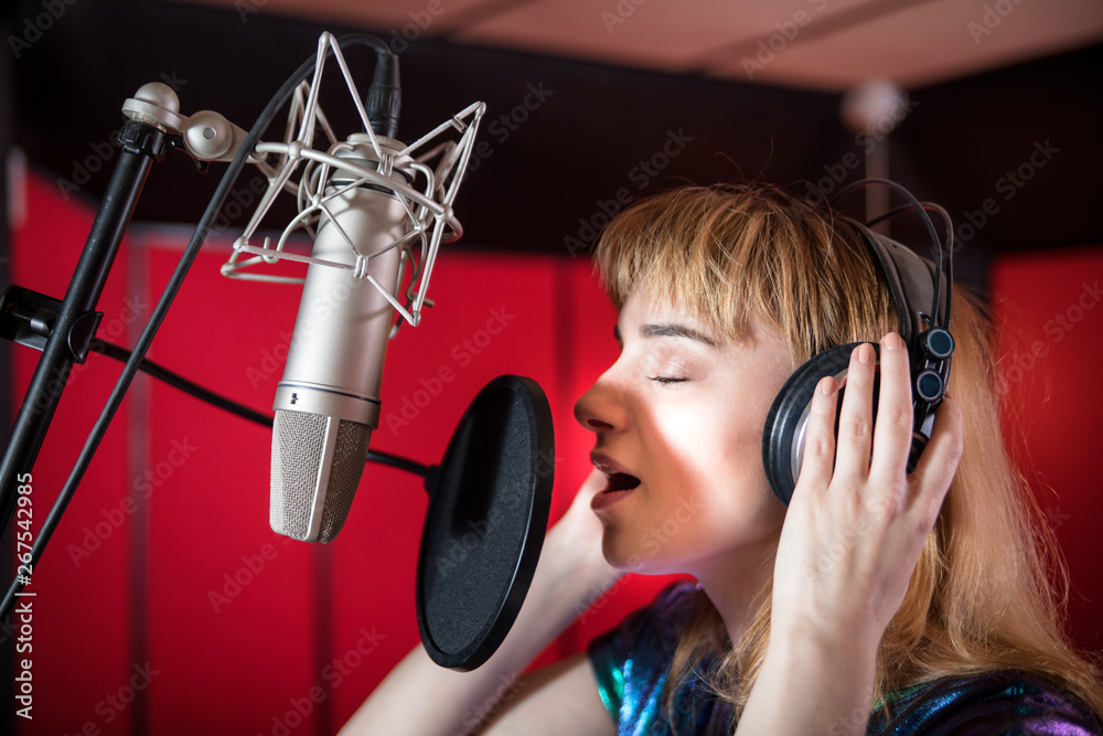 Pretty female singer recording voice in sound studio