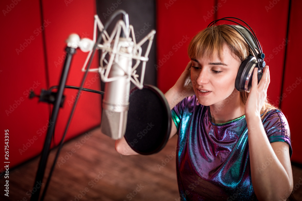 Pretty female singer recording voice in sound studio